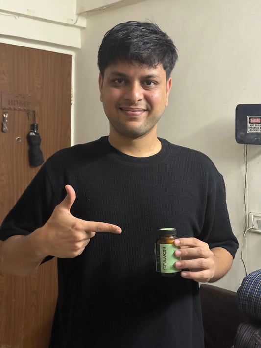 Man in black shirt smiling and pointing to a Seaamor supplement bottle indoors